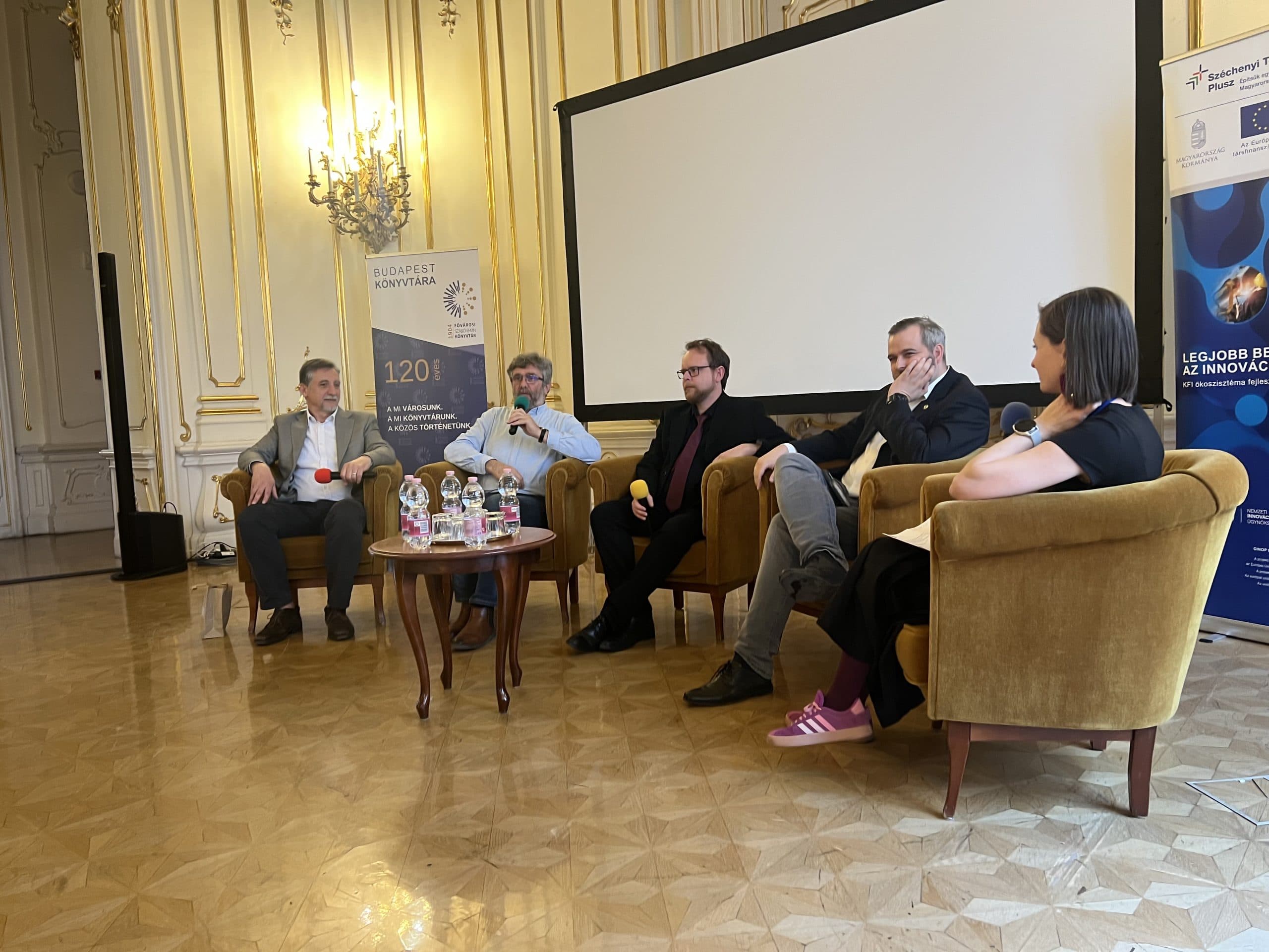 The five participants of the panel discussion seated in armchairs in front of the projection screen